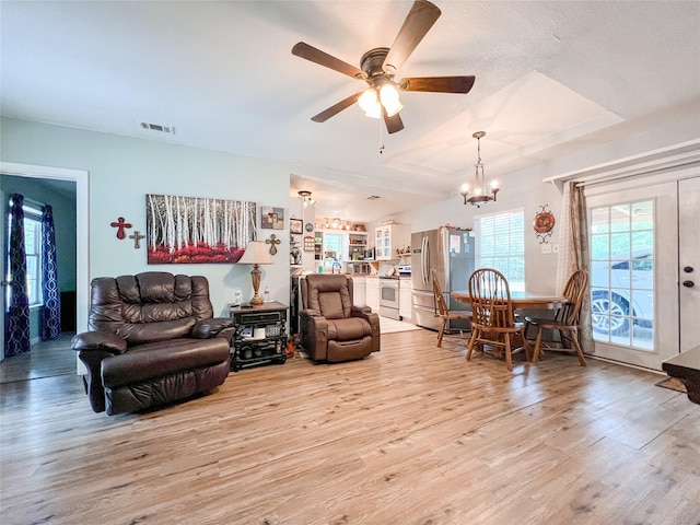 living room featuring light wood-style floors, visible vents, and ceiling fan with notable chandelier