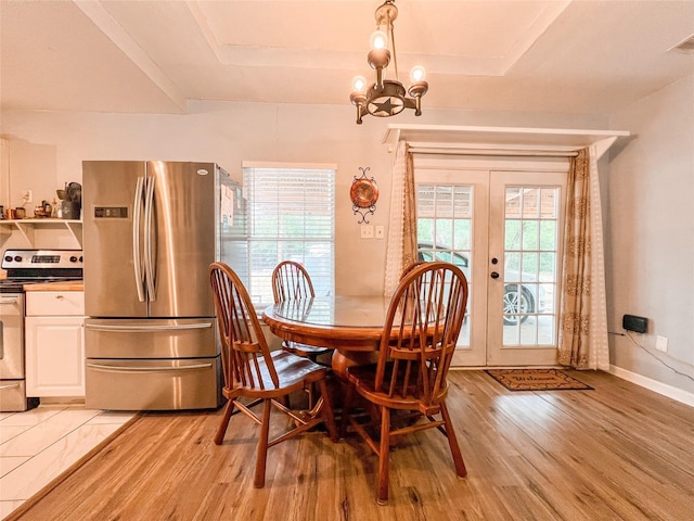 dining space with baseboards, a tray ceiling, french doors, light wood-type flooring, and a notable chandelier