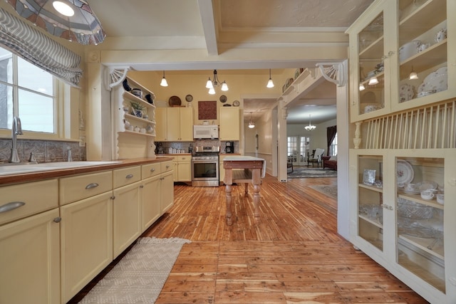 kitchen with beamed ceiling, tasteful backsplash, stainless steel range, light hardwood / wood-style flooring, and decorative light fixtures