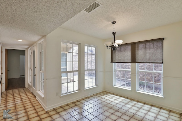 unfurnished dining area featuring a textured ceiling, an inviting chandelier, and plenty of natural light