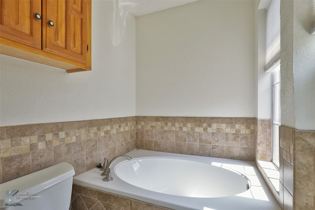 bathroom with a healthy amount of sunlight, toilet, tiled bath, and a textured ceiling