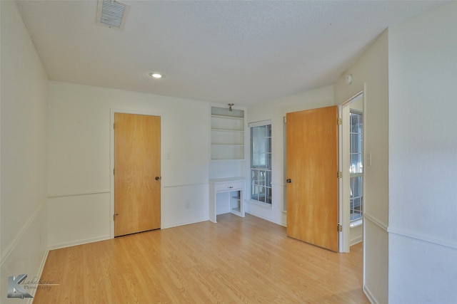 spare room featuring light hardwood / wood-style flooring and built in shelves