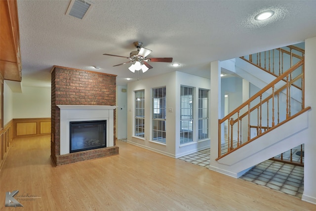 unfurnished living room with a textured ceiling, hardwood / wood-style flooring, ceiling fan, and a brick fireplace