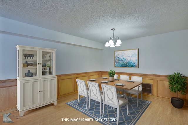 dining area with a notable chandelier, a textured ceiling, and light wood-type flooring