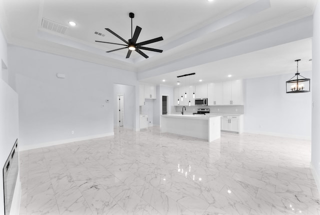 unfurnished living room with ceiling fan with notable chandelier, ornamental molding, a tray ceiling, and sink