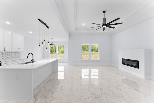 kitchen featuring hanging light fixtures, a large island with sink, white cabinetry, sink, and ceiling fan