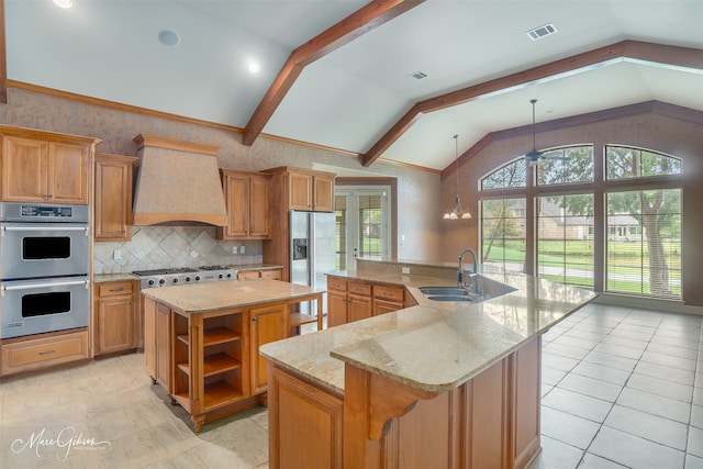 kitchen featuring light stone countertops, premium range hood, a kitchen island with sink, sink, and lofted ceiling with beams