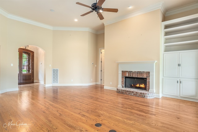 unfurnished living room featuring a fireplace, light hardwood / wood-style flooring, ceiling fan, ornamental molding, and a towering ceiling