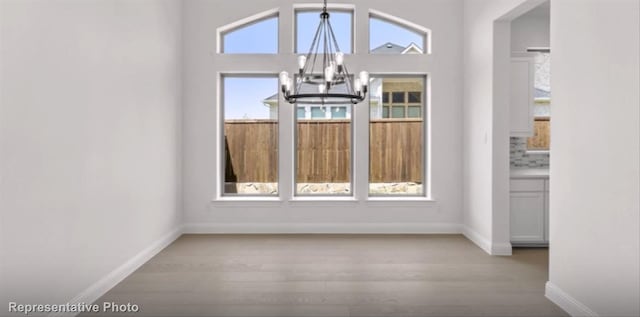 unfurnished dining area with baseboards, wood finished floors, a wealth of natural light, and a notable chandelier