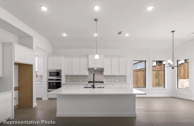 kitchen featuring under cabinet range hood, white cabinets, light countertops, appliances with stainless steel finishes, and an island with sink