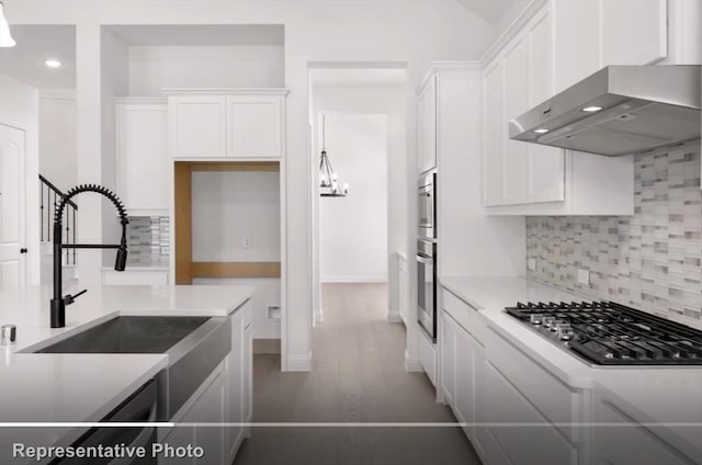 kitchen featuring stainless steel appliances, a sink, white cabinetry, wall chimney range hood, and tasteful backsplash