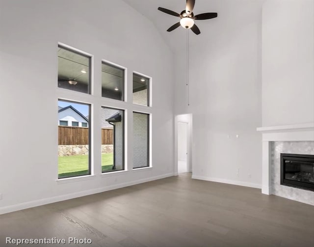 unfurnished living room featuring high vaulted ceiling, wood finished floors, baseboards, and a premium fireplace