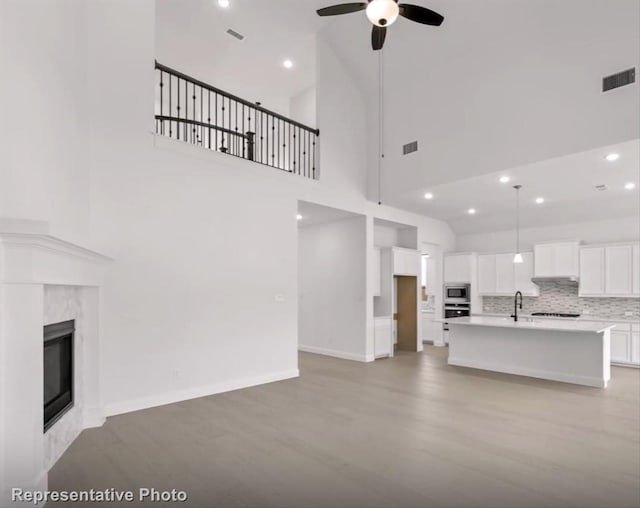 unfurnished living room featuring a towering ceiling, visible vents, a ceiling fan, and a high end fireplace