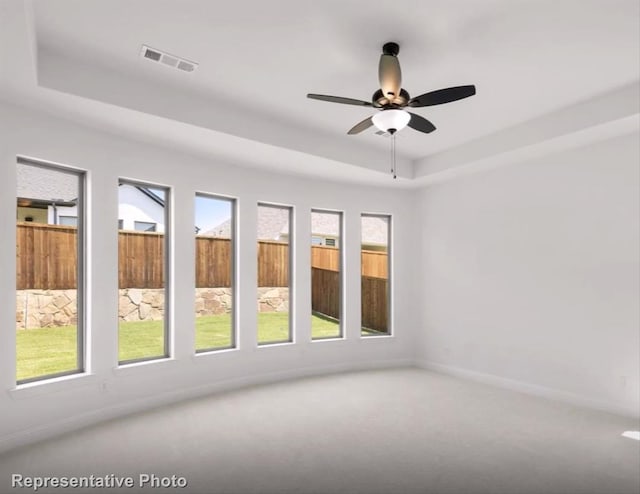 carpeted empty room with visible vents, a tray ceiling, and a wealth of natural light