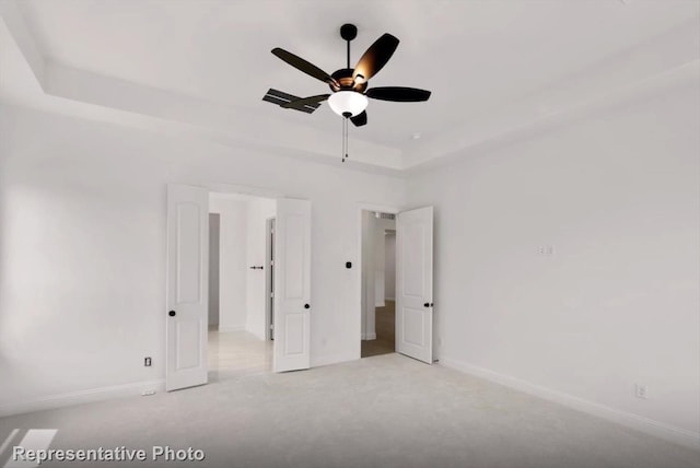 unfurnished bedroom with ceiling fan, carpet, a raised ceiling, and baseboards