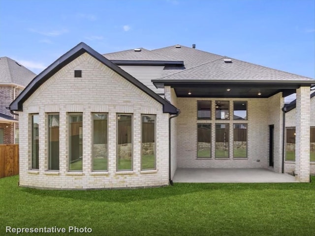 rear view of house with a lawn, a patio, roof with shingles, fence, and brick siding