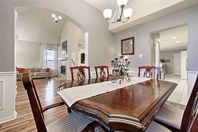 dining space featuring a fireplace, vaulted ceiling, light hardwood / wood-style flooring, and a notable chandelier