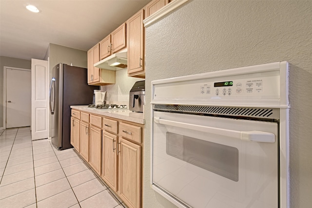 kitchen featuring stainless steel gas stovetop, light brown cabinets, light tile patterned flooring, and white oven