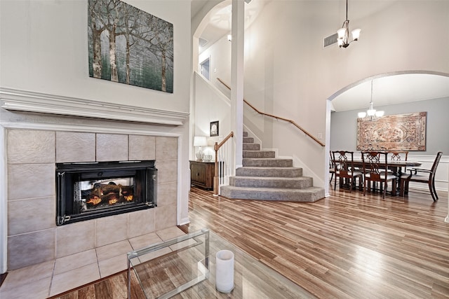 living room with a high ceiling, a tile fireplace, light hardwood / wood-style floors, and a notable chandelier