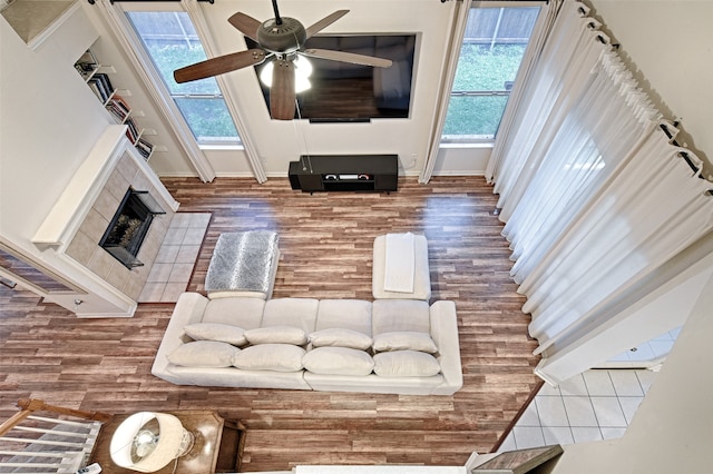 living room with hardwood / wood-style floors, ceiling fan, a tiled fireplace, and a healthy amount of sunlight