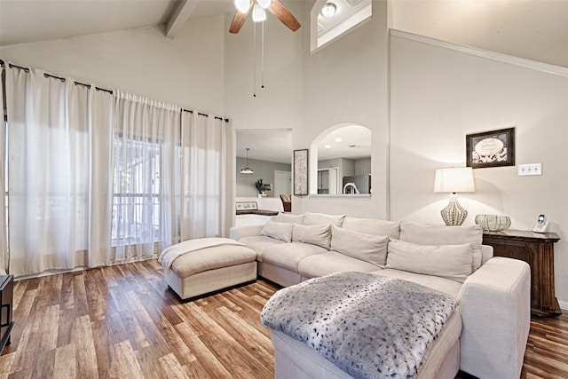 living room featuring high vaulted ceiling, ornamental molding, wood-type flooring, ceiling fan, and beam ceiling