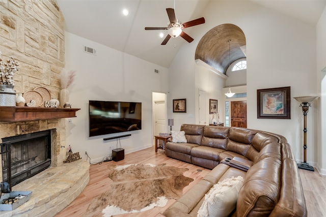 living room with high vaulted ceiling, a stone fireplace, ceiling fan, and light hardwood / wood-style flooring