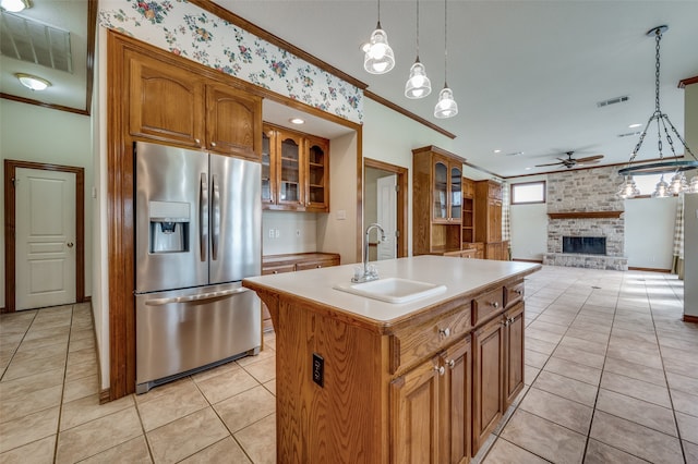 kitchen with ceiling fan with notable chandelier, a fireplace, stainless steel fridge with ice dispenser, a kitchen island with sink, and sink