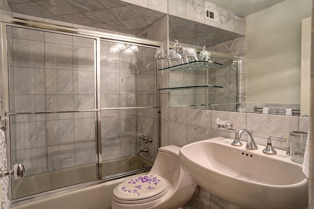 full bathroom with tile walls, toilet, sink, and bath / shower combo with glass door