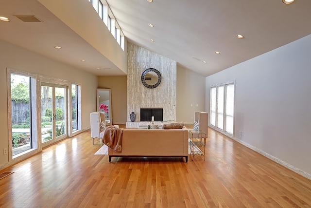 living room featuring light wood-type flooring, a large fireplace, high vaulted ceiling, and a wealth of natural light