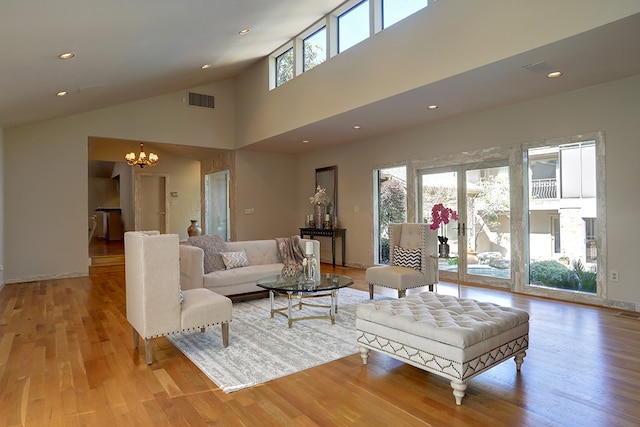 living room featuring light wood-type flooring, high vaulted ceiling, and a chandelier