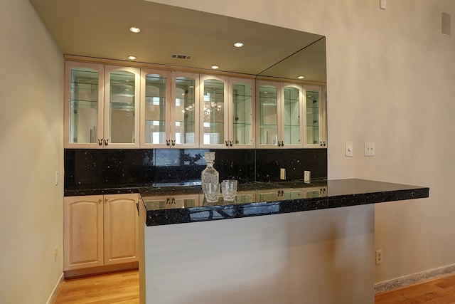 bar with dark stone counters, light hardwood / wood-style flooring, and backsplash