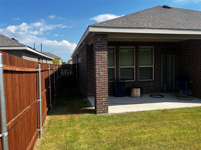 view of side of home with brick siding, a lawn, fence, and roof with shingles