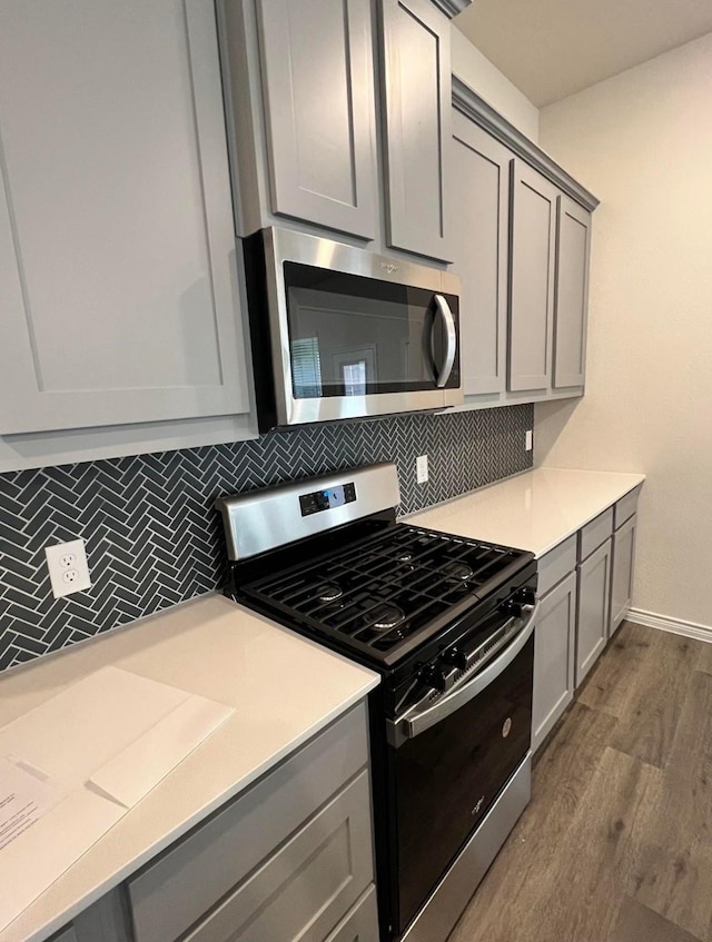kitchen featuring gray cabinetry, dark wood-style floors, appliances with stainless steel finishes, and tasteful backsplash
