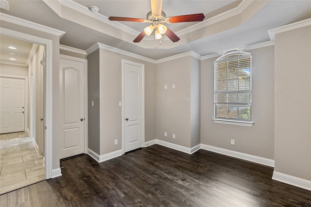 unfurnished bedroom with ceiling fan, a raised ceiling, dark hardwood / wood-style floors, and crown molding