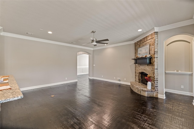 unfurnished living room with crown molding, a stone fireplace, dark wood-type flooring, and ceiling fan