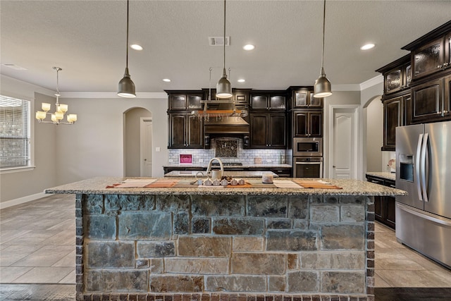 kitchen with dark brown cabinets, appliances with stainless steel finishes, hanging light fixtures, and a center island with sink