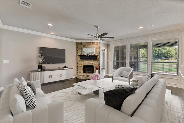 living room featuring dark wood-type flooring, a stone fireplace, a textured ceiling, and crown molding