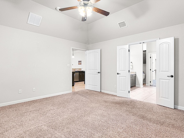 unfurnished bedroom featuring ceiling fan, connected bathroom, light carpet, and vaulted ceiling