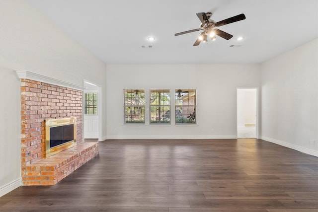 empty room with a fireplace, ceiling fan, and dark wood-type flooring