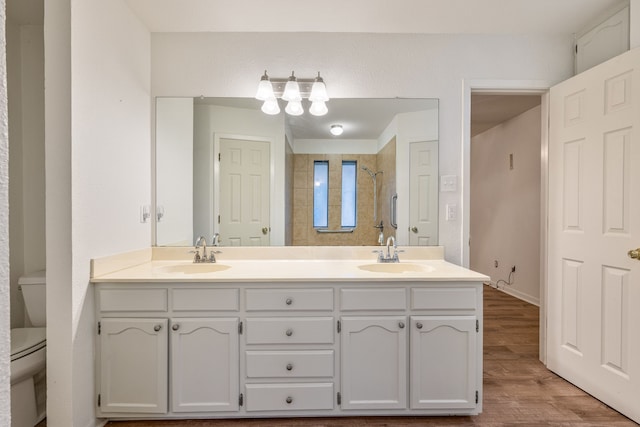 bathroom with wood-type flooring, vanity, a tile shower, and toilet