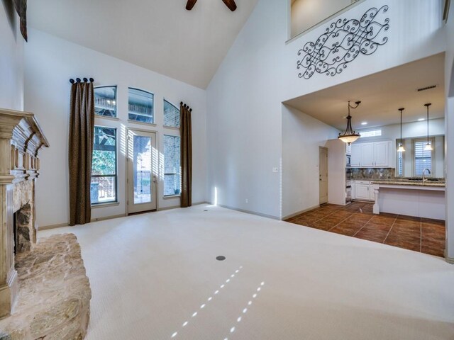 unfurnished living room with a fireplace, dark tile patterned flooring, ceiling fan, sink, and high vaulted ceiling