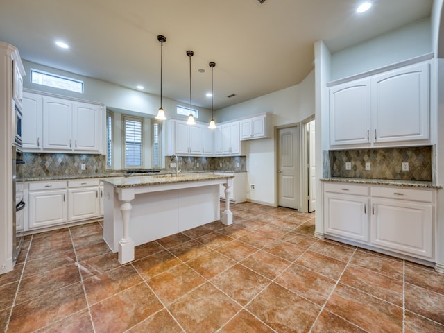 kitchen featuring a kitchen island, light stone countertops, decorative backsplash, and white cabinetry