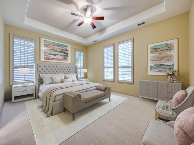 bedroom with a tray ceiling, light colored carpet, and ceiling fan