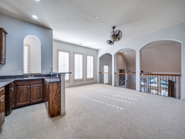 kitchen featuring light colored carpet, sink, dark brown cabinetry, and dark stone counters