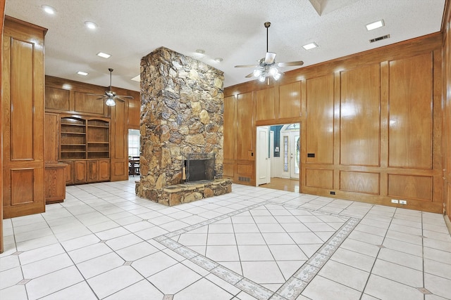 unfurnished living room featuring ceiling fan, a textured ceiling, and a stone fireplace