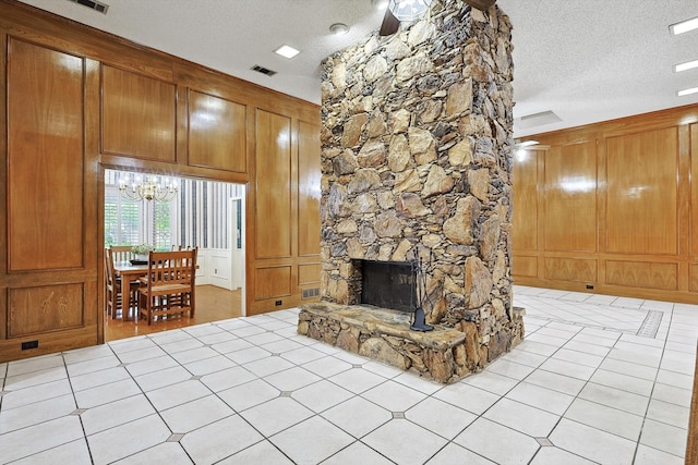 living room featuring ceiling fan with notable chandelier, light tile patterned floors, a fireplace, and a textured ceiling