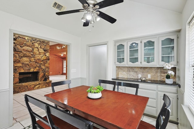 dining room with plenty of natural light, ceiling fan, vaulted ceiling, and a fireplace