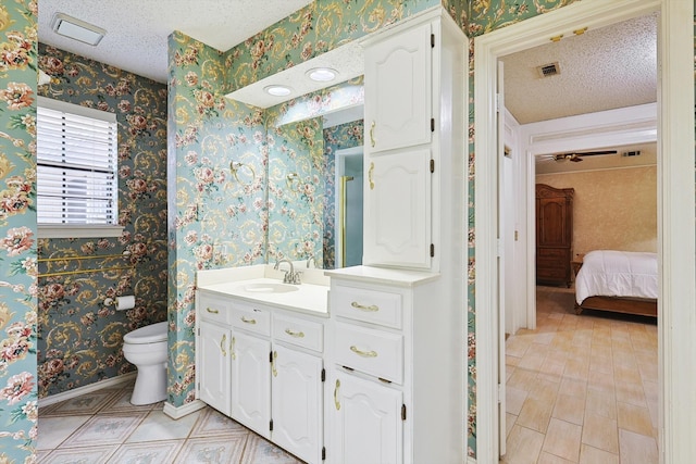 bathroom with a textured ceiling, vanity, toilet, and ceiling fan