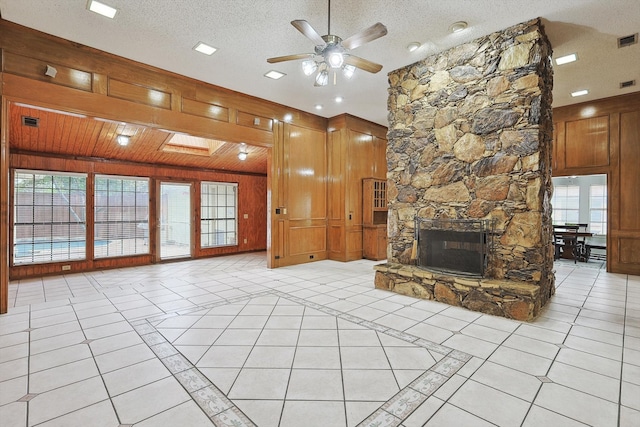 unfurnished living room with wooden walls, a textured ceiling, ceiling fan, a stone fireplace, and light tile patterned flooring