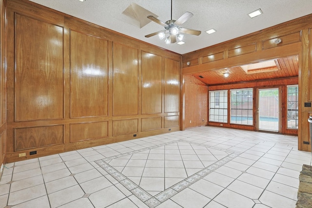 unfurnished room with lofted ceiling with skylight, wooden walls, a textured ceiling, light tile patterned floors, and ceiling fan